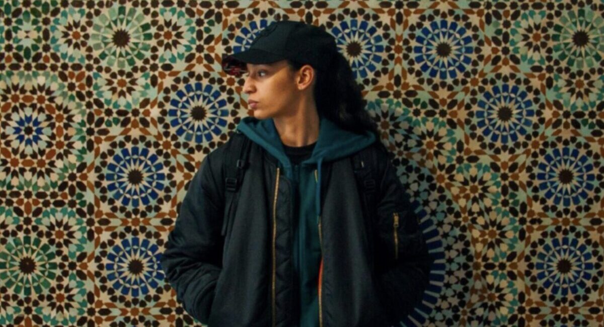 Woman in baseball cap standing against patterned backdrop